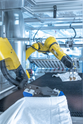 在 IDS 2D 和 3D 摄像头的帮助下，两个机器人在工业洗衣房内展开衣物。